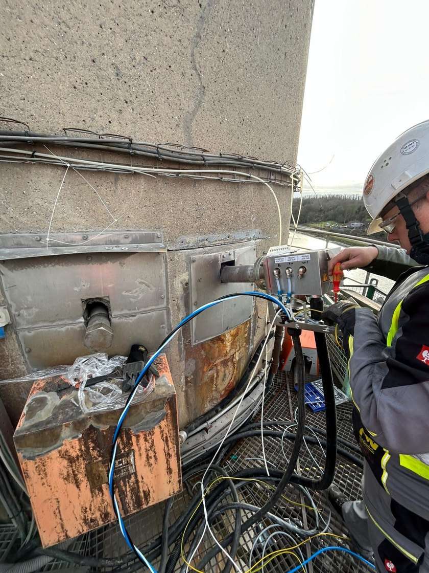 Technicien en équipement de protection individuelle raccordant une sonde de prélèvement chauffée sur le conduit d'une cimenterie.